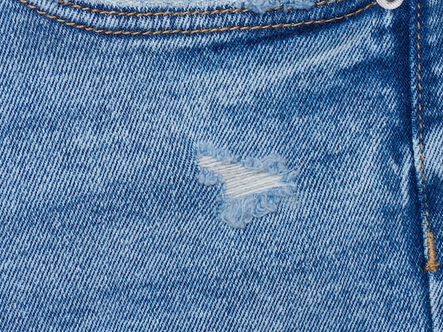 Fragment of blue jeans fabric with a hole full frame close up