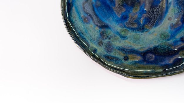 Fragment of a ceramic plate with stains of blue and green glaze on a white background