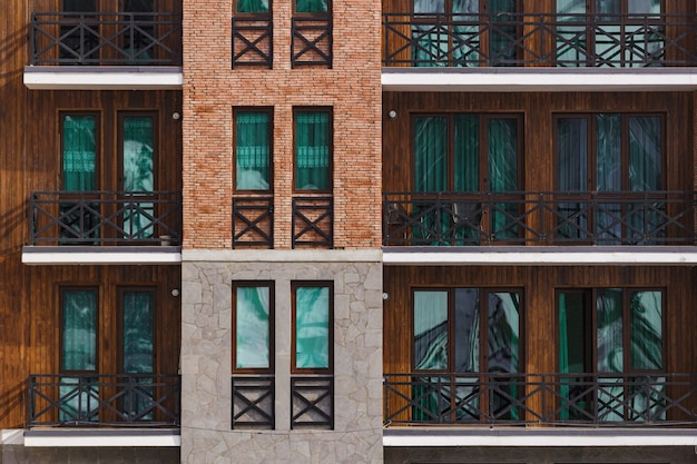 Fragment of a facade of a building with tall windows and balconies. Modern home with many flats.