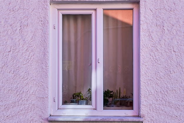 Frammento di facciata di villa di campagna con finestra in plastica color lilla e parete intonacata con stucco grezzo dipinto in viola