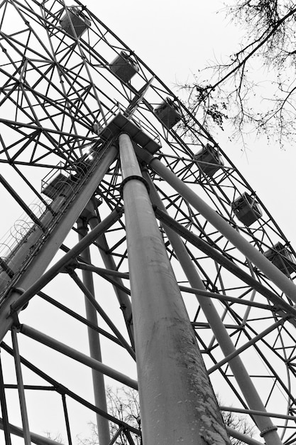 Photo fragment of a ferris wheel, visible through the branches of winter trees in a misty gloomy evening weather