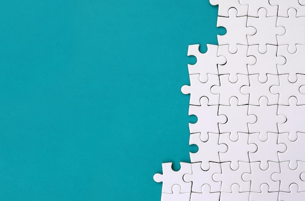 Fragment of a folded white jigsaw puzzle on the background of a blue plastic surface