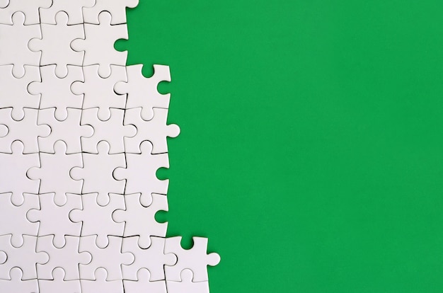 Fragment of a folded white jigsaw puzzle on the background of a green plastic surface