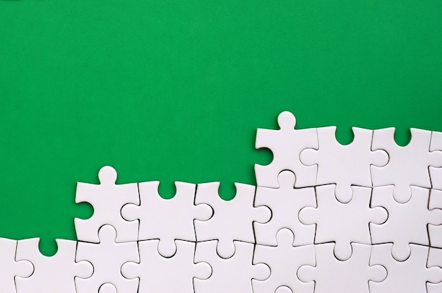 Fragment of a folded white jigsaw puzzle on the background of a green plastic surface