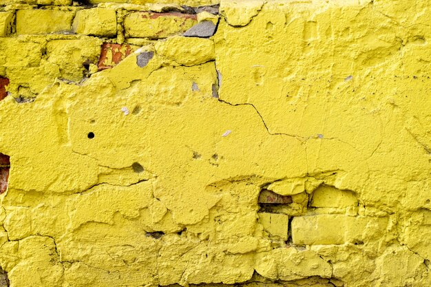 거친 석고와 밝은 노란색 벽돌로 된 오래된 벽 조각
