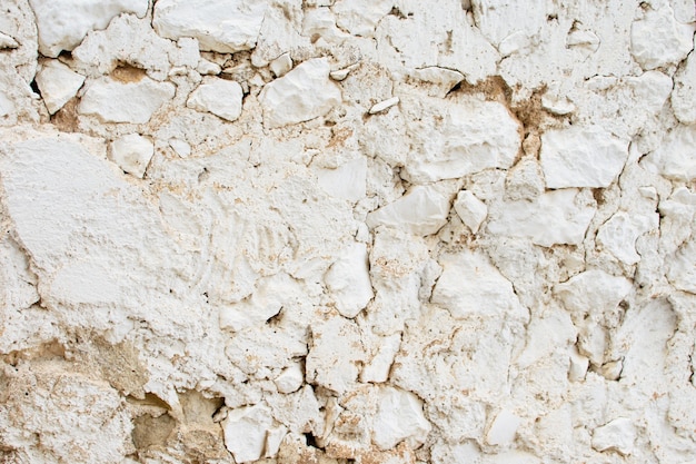Fragment of an old white stone wall with large stones and cracked plaster. Great for design and texture background.