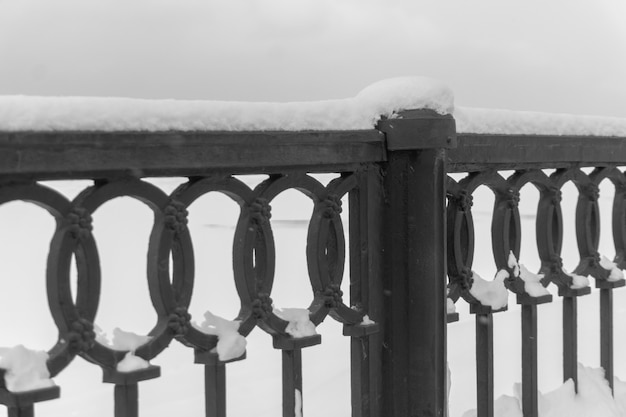 fragment of a snowcovered patterned castiron fence on the embankment