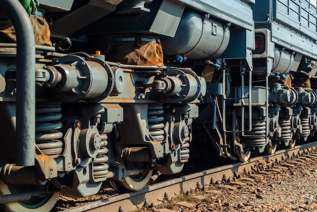 Frammento di una locomotiva moderna illuminata dal sole su un binario con telai di camion che si estendono in prospettiva