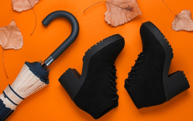 Fragment of umbrella hook, boots and fallen leaves on orange background. Top view. Autumn accessories. Flat lay
