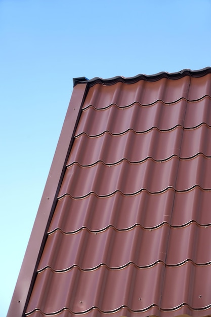 Foto fragment van het dak van een landhuis van bruine metalen tegels onder heldere wolkenloze blauwe hemel verticaal zicht