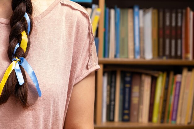 A fragment of a woman's braid with a yellowblue ribbon on the background of books