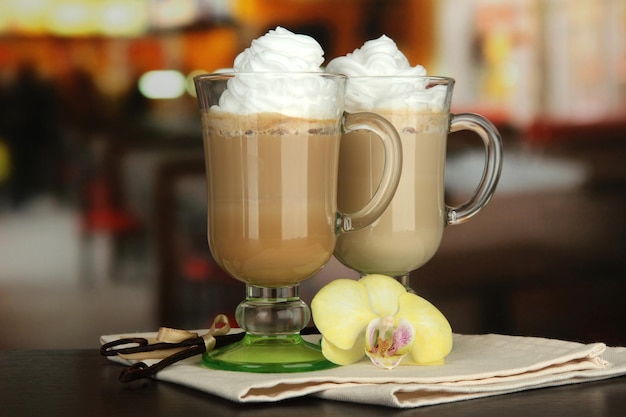 Fragrant coffee latte in glasses cups with vanilla pods on table in cafe