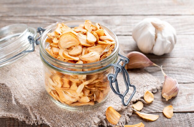 Fragrant dry garlic in flakes in a glass jar on an old wooden background, close-up