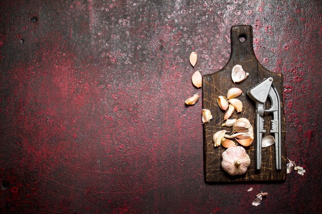 Fragrant garlic with a press tool on wooden Board on rustic table.