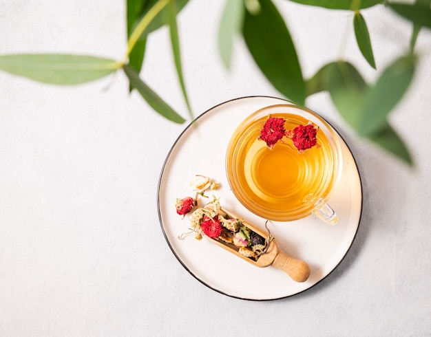 Fragrant herbal tea with pomegranate flowers in a glass cup on a plate on a white background with eucalyptus branches The concept of a healthy drink for breakfast