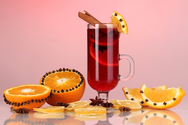 Fragrant mulled wine in glass with spices and oranges around on red background