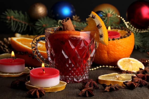 Fragrant mulled wine in glass with spices and oranges around on wooden table