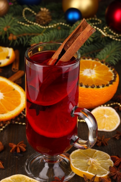 Fragrant mulled wine in glass with spices and oranges around on wooden table