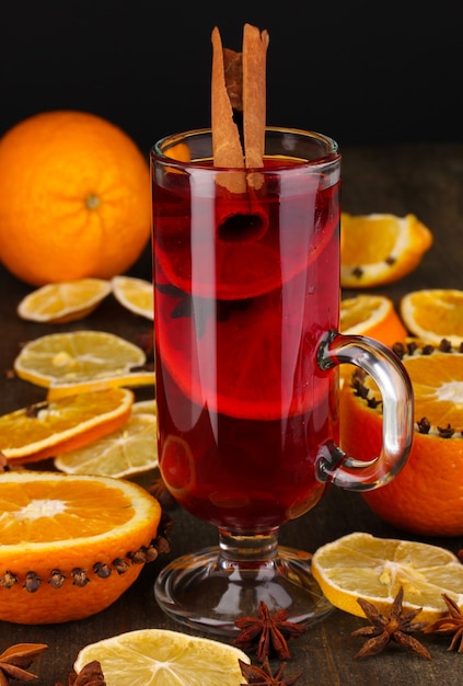 Fragrant mulled wine in glass with spices and oranges around on wooden table