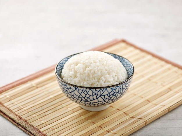 회색 배경에 나무 매트 측면 보기에 고립 된 향기로운 쌀 ina 그릇