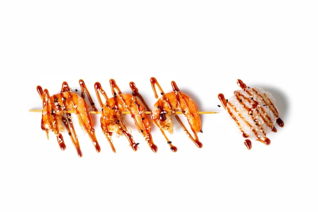 Foto gamberetti profumati su un bastoncino di legno accanto a un cerchio di riso guarnito con semi di sesamo e salsa teriyaki vista dall'alto piatto culinario per il menu del ristorante