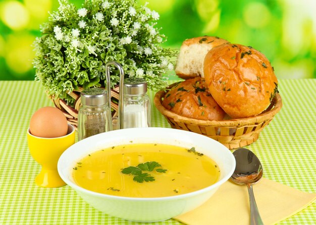 Fragrant soup in white plate on green tablecloth on natural background closeup