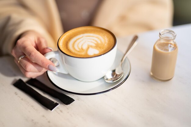 A fragrant and warm mug of cappuccino with a drawing heart girl hold in hands