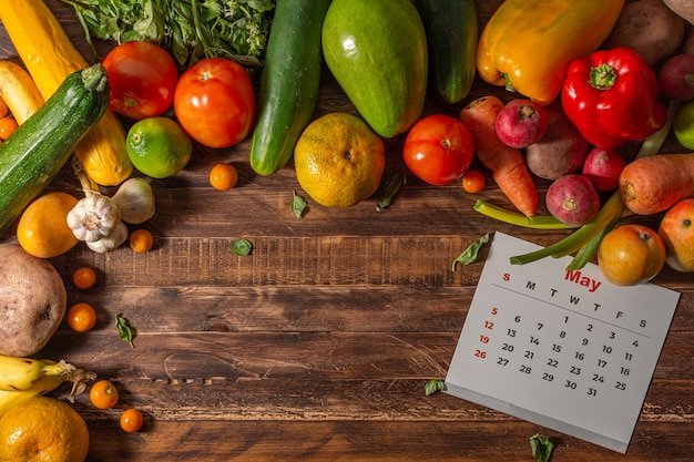 Frame of assorted fresh fruits and vegetables and calendar in\
english language on wooden background