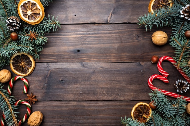 Frame of Christmas tree cones oranges caramel cane nuts on dark wooden background. Copy space. Flat lay.