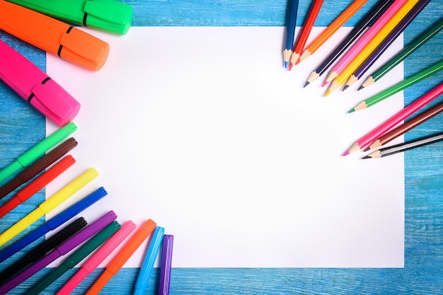 Frame of colored pencils around a white sheet on a wooden background