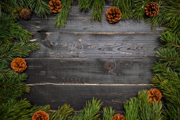 Frame of coniferous branches and cones on a black wooden