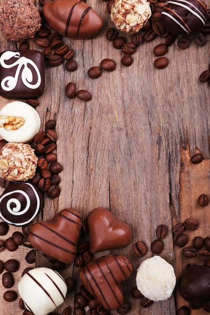 木製の織り目加工の背景にコーヒー豆とさまざまなチョコレートのフレーム