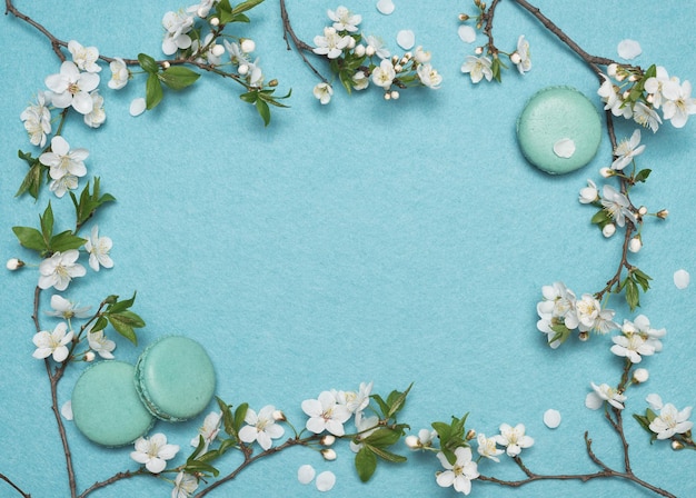 Frame of flowers and French macaroon dessert on a turquoise background