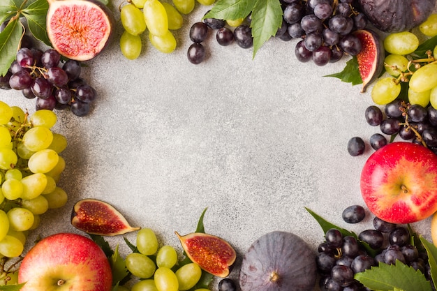 Frame of fresh autumn fruits. Grapes black and green, figs and leaves on a grey table with copy space.