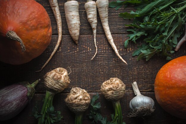 Frame from the roots of parsley celery with leaves and pumpkin on brown boards