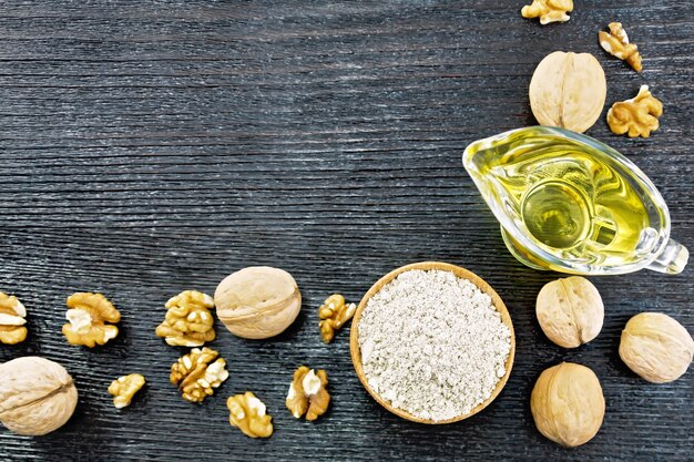 Frame from walnut flour in a bowl, oil in sauceboat and nuts on a black wooden board from above