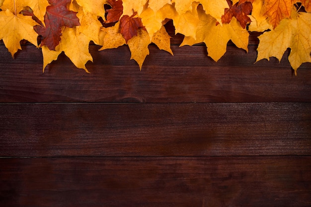 Frame from yellow autumn leaves on a brown wooden background Fallen foliage Backdrop for design