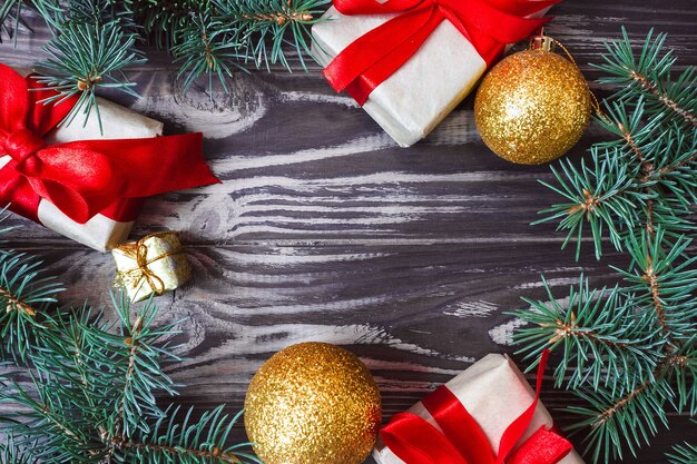 Frame of gift boxes of christmas decorations with red bows, toys and fir branches on a wooden background. postcard. copy space. flat lay. view from above