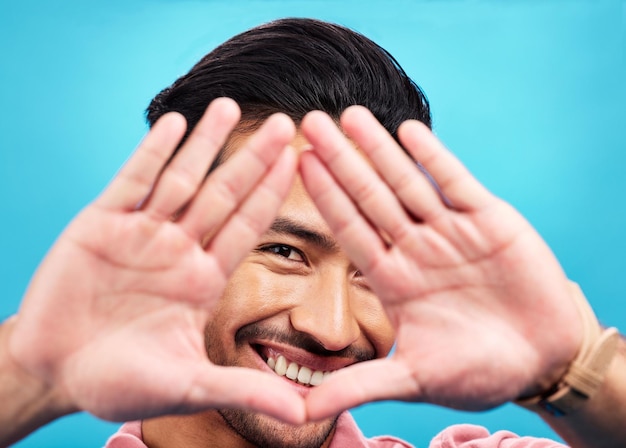 Фото Рамка руки и портрет счастливого азиатского мужчины на синем фоне с улыбкой уверенной и счастливой перспективная форма и лицо мужчины в студии для фотографии профиля и видения