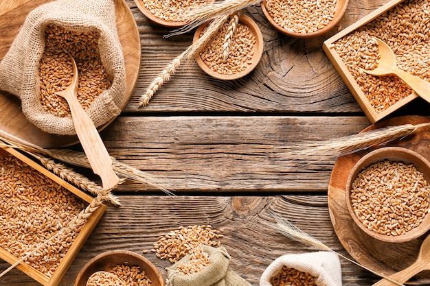 Frame made of bowls and bags with wheat grains on wooden background