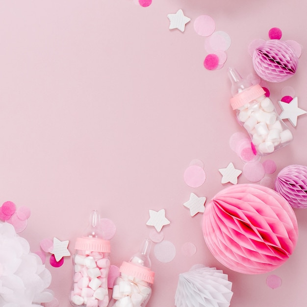 ベビーシャワーパーティー用のキャンディーと紙の装飾が施された装飾的なベビーミルクボトルで作られたフレーム。フラットレイ、上面図