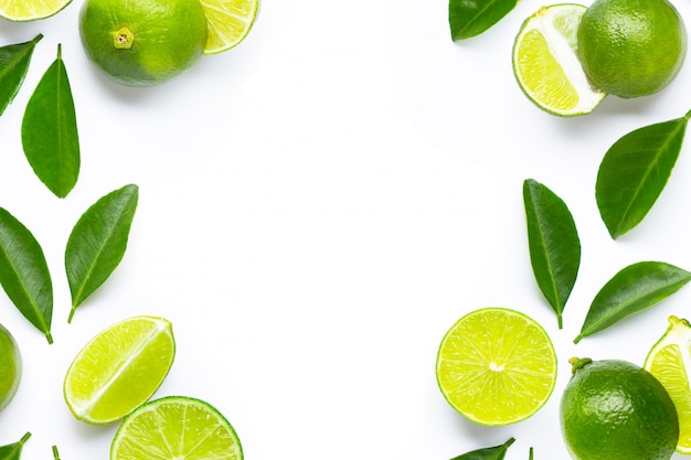 Frame made of fresh limes with green leaves on white background.