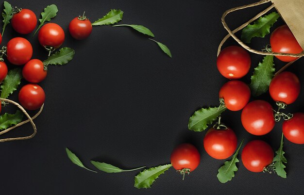 Frame made of red tomatoes and herbs on the black background Two paper bags with fresh red tomatoes