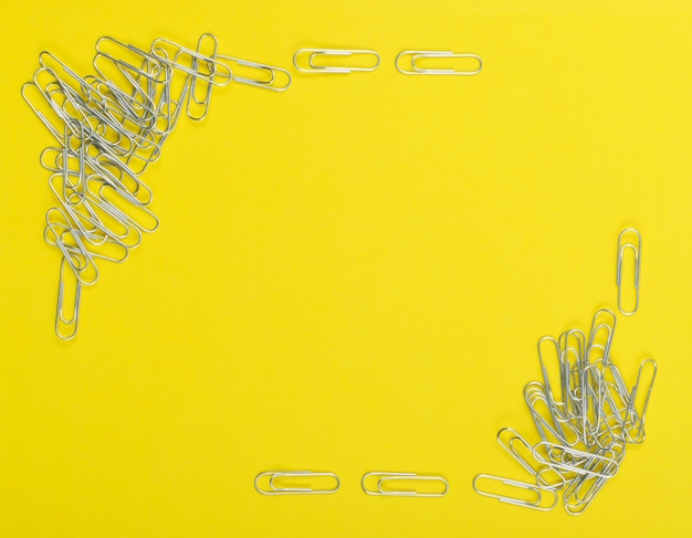 Frame of note paper clips on yellow background top view. Pile of steel clips or paperclips close up