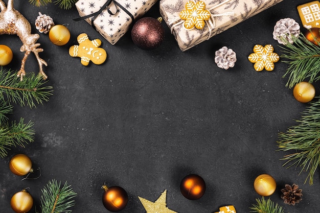 공, 소나무 콘, 가문비나무 가지가 있는 크리스마스 선물 프레임이 어두운 배경 상단에 있습니다. 플랫 레이. 크리스마스와 새 해 휴일 배경입니다. 크리스마스 인사말 카드 개념
