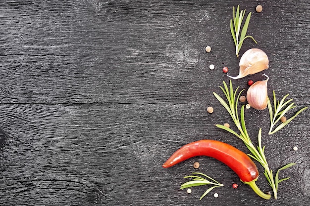 Frame of peas of colored pepper, fresh rosemary, pod of red hot\
pepper and two cloves of garlic on a black wooden board top