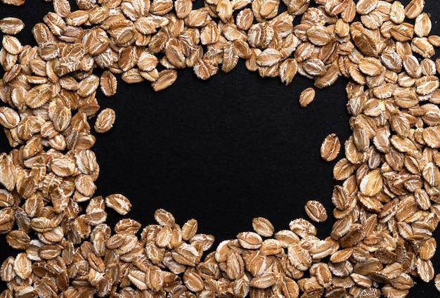 Frame of rye flakes on black , top view