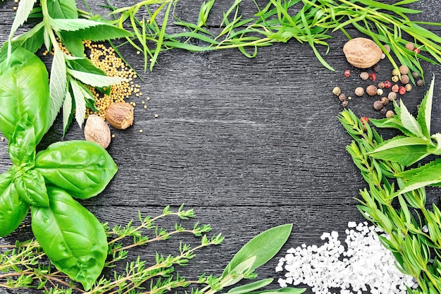 Frame of savory leaves, tarragon, sage, basil and thyme, salt, nutmeg, mustard seeds and pepper on the background of wooden boards