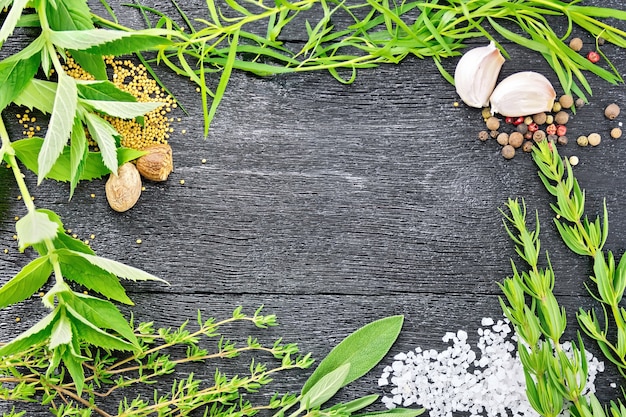 Frame of savory leaves, tarragon, sage and thyme, salt, nutmeg, mustard seeds, pepper and garlic on the background of wooden boards