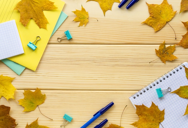 Frame of school or office stationery with maple leaves on a light wooden background. Space for text.